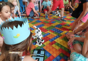Na zdjęciu widać grupę dzieci na dywanie, które wykorzystują aplikację " Brain it on" do działań robota
